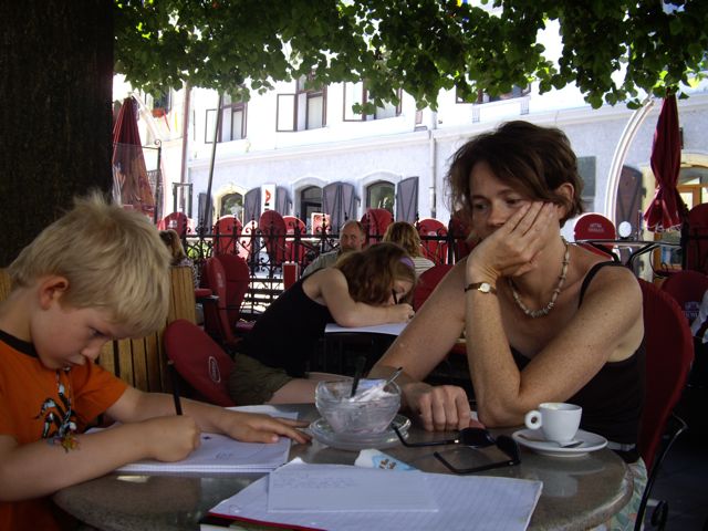 Balder fordybet i at tegne ved rundt cafébord, mens mor kikker på. I baggrunden Synnøve.